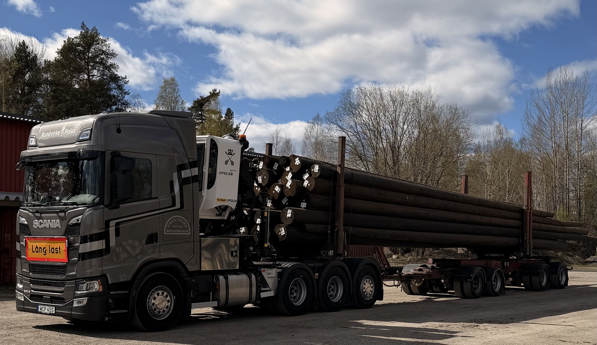 Scania med lång last av stolpvirke på utdraget ekipage